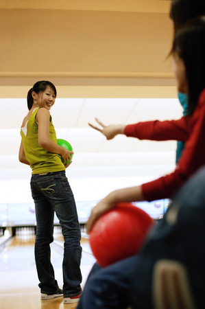 Three women at a bowling alley, one woman with bowling ball, looking over shoulderの写真素材