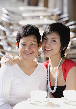 Mother and adult daughter in cafe, smiling at camera, portraitの写真素材