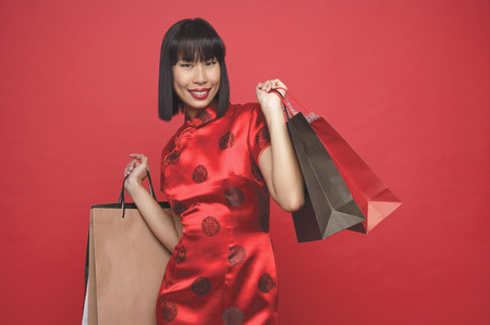 Woman in red cheongsam with shopping bagsの写真素材