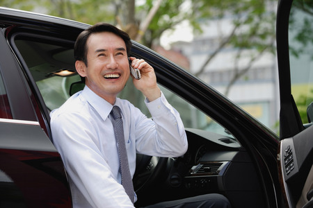 Businessman sitting in car, using mobile phone, smilingの写真素材