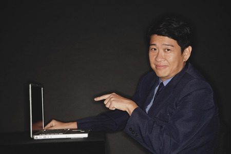 Businessman pointing at laptop, looking at camera