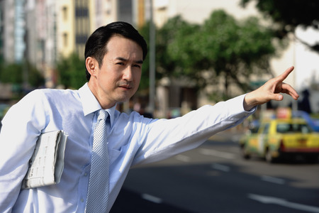 Businessman with newspaper under his arm, flagging a cabの写真素材