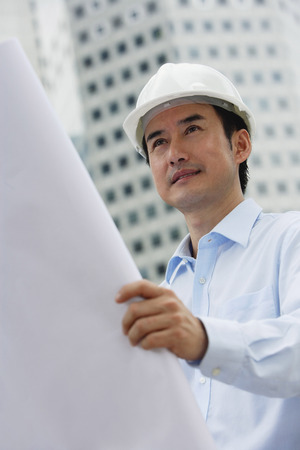 Man in hardhat, holding blueprintsの写真素材