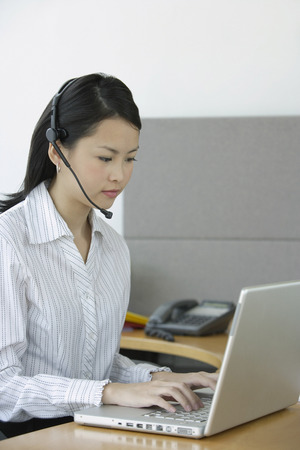Young woman using laptop, wearing hands free deviceの写真素材