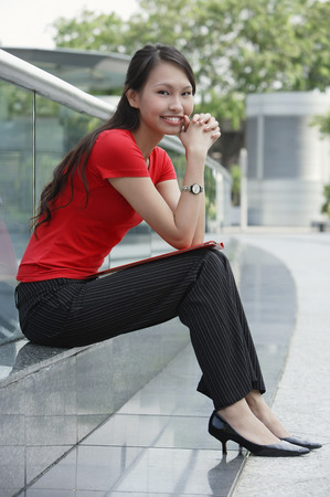 Young woman sitting on ledge outdoors, smiling at cameraの写真素材