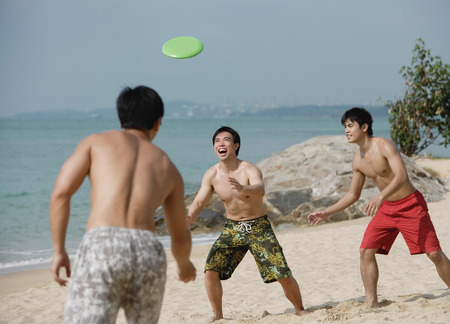 Three young men on beach playing with Frisbeeの写真素材