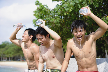 Three men sitting side by side, pouring water on themselvesの写真素材