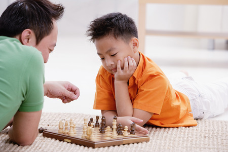 Father and son lying on floor, playing chessの写真素材