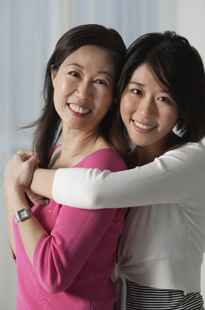Mother with grown daughter, embracing, looking at cameraの写真素材