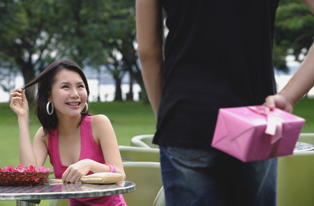 Woman seated at table, man in foreground holding gift behind his backの写真素材