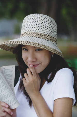 Young woman wearing hat, holding book, finger on mouthの写真素材