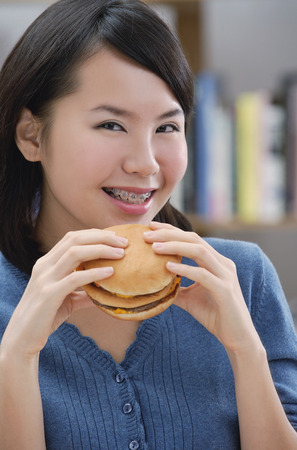 Young woman eating a burger, smilingの写真素材