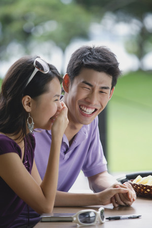 Couple sitting at cafe, young woman with hand over mouth, smilingの写真素材