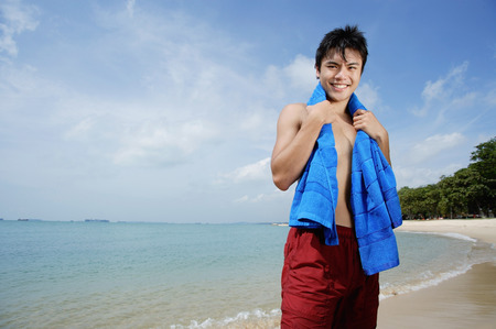 Man standing on beach, holding towel around his neckの写真素材