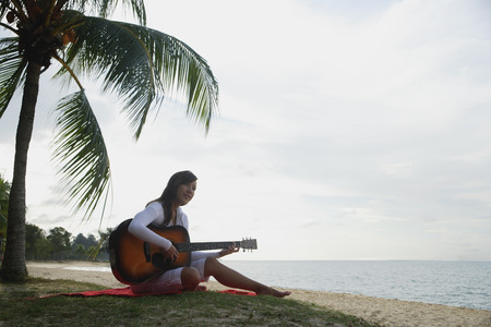Young woman sitting on beach with a guitar