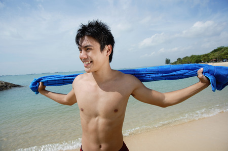 Man standing on beach, holding towel, looking awayの写真素材