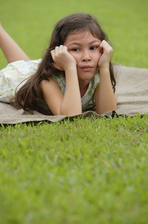 Girl lying on picnic blanket, hands on face, sad expressionの写真素材
