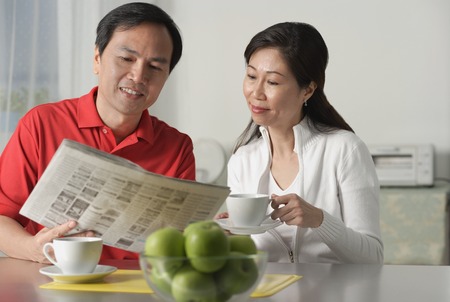 Mature couple at home, looking at newspaper and having coffeeの写真素材