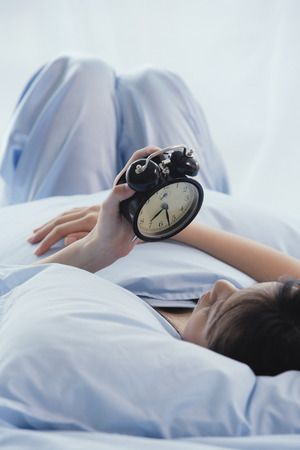 Young woman lying on bed, looking at alarm clockの写真素材