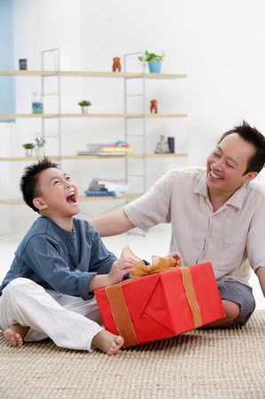 Father and son at home, boy opening gift, looking upの写真素材