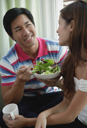 Couple talking, man eating a salad, woman holding a mugの写真素材
