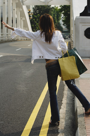 Woman standing by road, waving for taxi, rear viewの写真素材