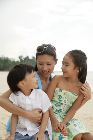 Mother, daughter and son sitting on beach togetherの写真素材