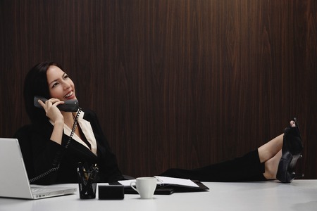 A woman talks on the phone while she is at her deskの写真素材
