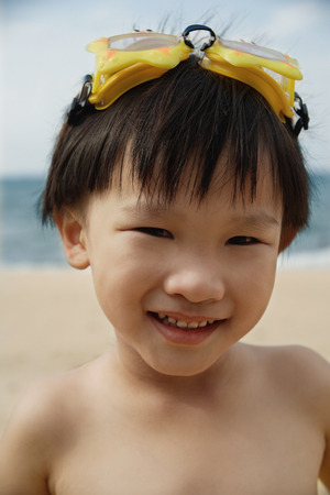 Young boy on beach with yellow swimming goggles on head, smiling, portraitの写真素材