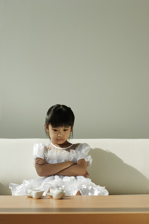 Girl sitting on sofa with tea set on coffee tableの写真素材