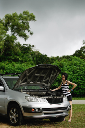 A woman checks under the hood of her carの写真素材