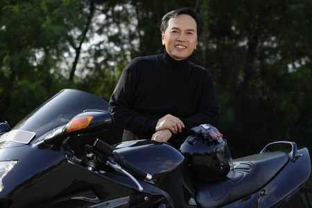 Man standing by black motorcycle, smiling at cameraの写真素材