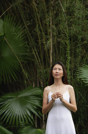 Woman standing outdoors, looking up, hands claspedの写真素材