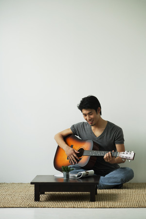 Young man sitting on floor and playing guitarの写真素材