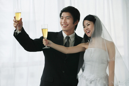 A newlywed couple hold out their champagne glasses for a toastの写真素材