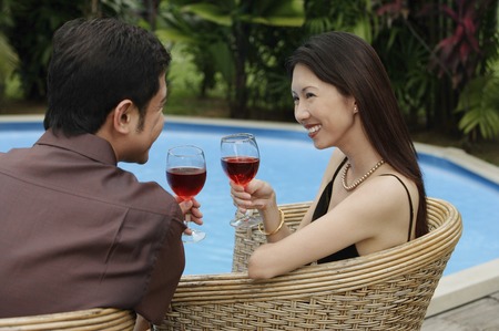 Couple sitting by swimming pool, holding wine glassesの写真素材