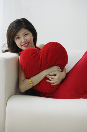 Young woman sitting on sofa with heart-shaped cushionの写真素材