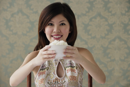 Young woman raising bowl of rice smiling at cameraの写真素材