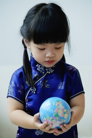 A small girl in blue silk cheongsam holds a globeの写真素材