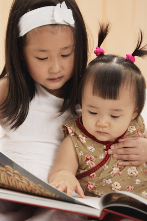 Baby girl with older sister, reading book togetherの写真素材