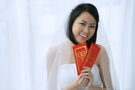 A bride smiles at the camera and holds out two red envelopesの写真素材
