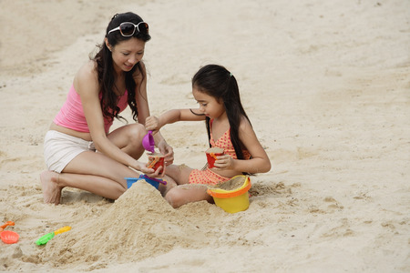 Mother and daughter building sand castle on beachの写真素材