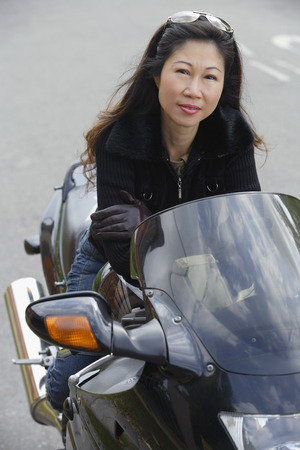 Mature woman sitting on motorcycle, smiling at cameraの写真素材