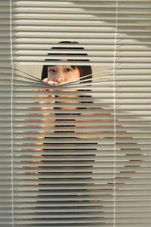 Young woman behind Venetian blindsの写真素材