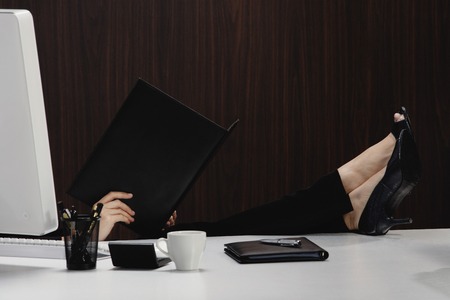 A woman puts her feet up on her desk as she reads from a folderの写真素材
