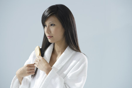 woman wearing bathrobe, brushing hair and looking away from cameraの写真素材
