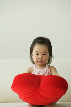 Baby girl with heart-shaped cushionの写真素材