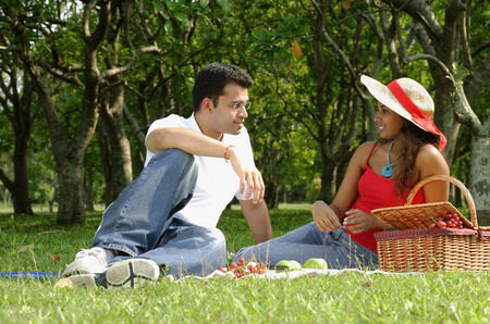 Couple in park, sitting on grass, having picnicの写真素材