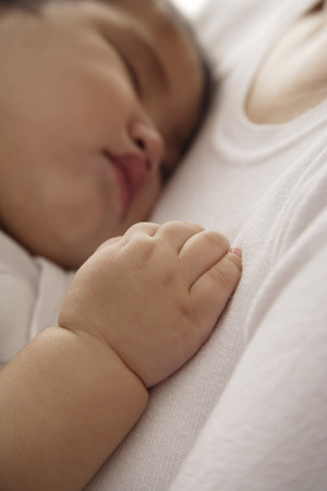 baby girl sleeping against woman's chestの写真素材