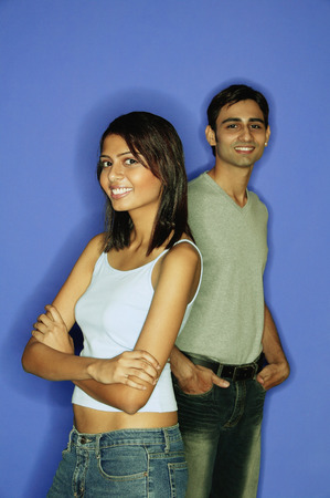 Woman standing in front of man, arms crossed, man behind with hands in pocketの写真素材